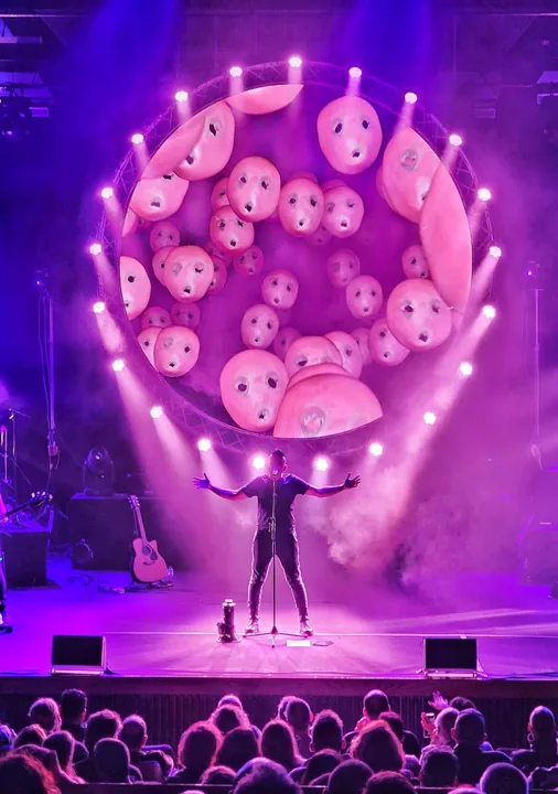 The singer with arms outstretched beneath a round screen filled with faces